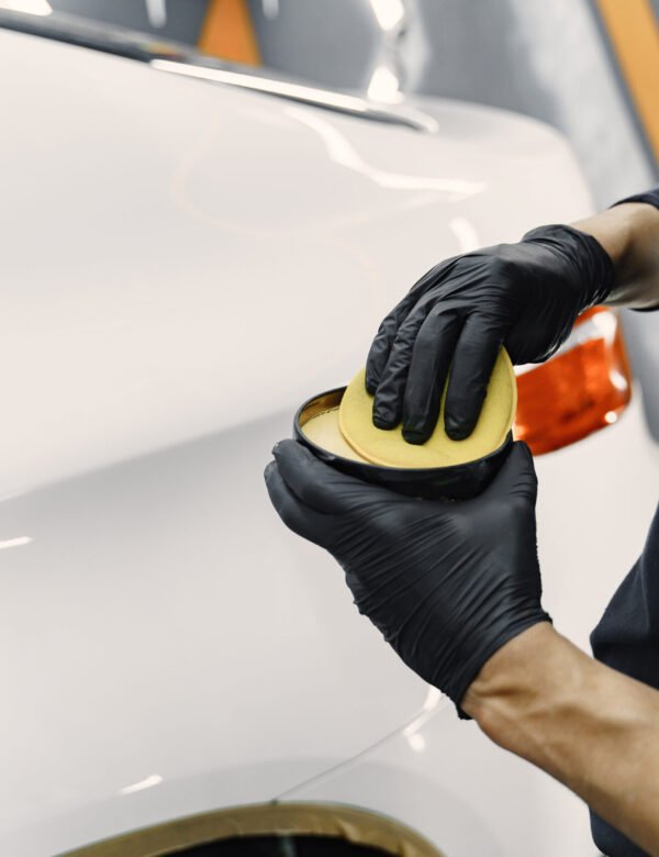 Man in a garage. Worker polish a car. Man in a black uniform.